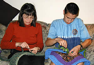 Woman and young man sit together on a couch (Diane Fields at left, Mitchell Fields right) working on rugs.