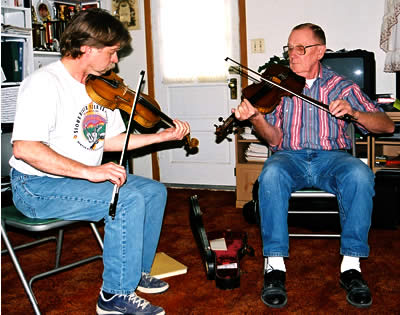 Two men, seated together in a room (Bill Peterson at left, Dwight Lamb at right) play fiddle. 