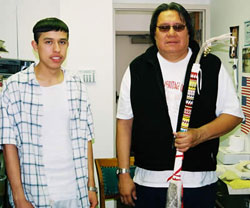 Two men (Calvin Renteria at left and Alvin Pipe on Head) standing together. Alvin hopes a beaded Deer Dance stick.