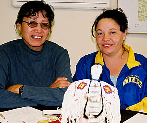 Two women (Tilda St. Pierre at left and Stephanie Sorbel) sitting. Sorbel presents beaded lakota doll.