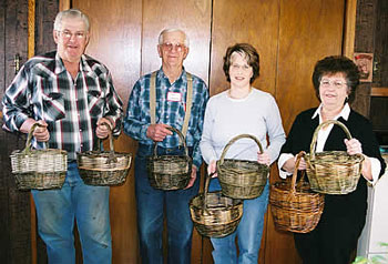 Two men stand at left of two women each holding willow baskets. 
