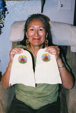 Women (Belinda Joe) sits and presents a pair of moccasin tops.