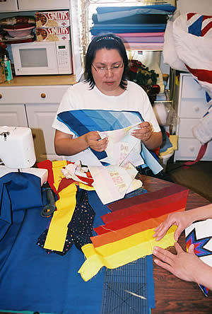 Woman (Renee Turning Heart) sits at table with quilting fabric and tools