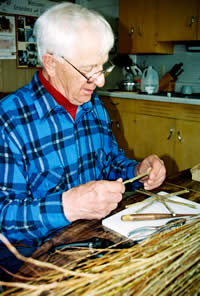 Man (LeRoy Graber) seated at work bench selecting willows.