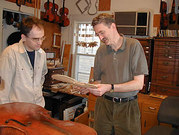 Chris Unversagt and John Waddle (two men) study a violin piece in shop.