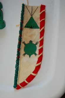 Rawhide knife sheath with red and green beading around edge, beaded turtle shape, beaded tipi shape