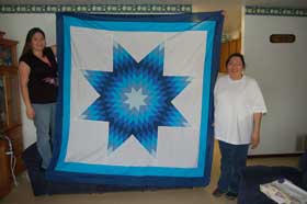 Two women holding a blue toned star quilt. Kristen Turning Heart at left. Renee Turning Heart at right. 