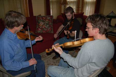 Three men play fiddles in interior of house. Master Bill Peterson (at left), Apprentices Nathan Glazier and Josh Scott.