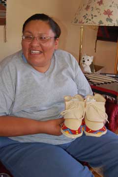 Women (Apprentice Vanessa Brings Him Back) seated with pair of moccasins, beaded across toes, on her lap.