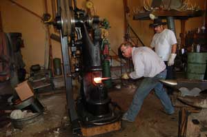 Man (Kevin Willey) forges a steel knife while another man (teacher Shane Taylor) watches.