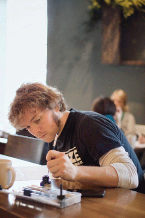 Artist sitting at a table in a cafe, focusing on a project in front of them, with a coffee mug nearby.