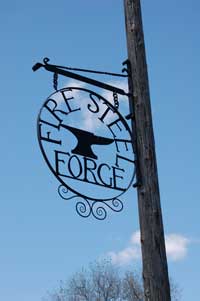 Metal sign on street post, reads "Fire Steel Forge."